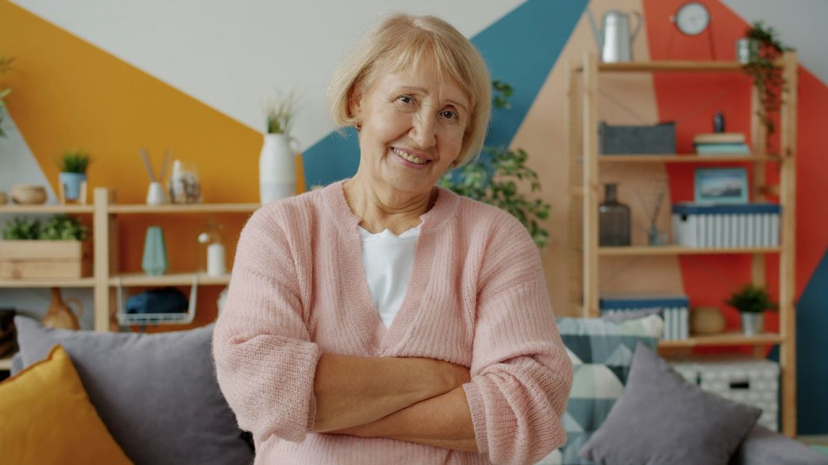 An older woman smiling with her arms crossed in her living room